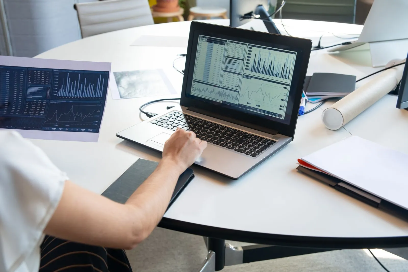 Person working on a laptop with market data charts next to a printed report